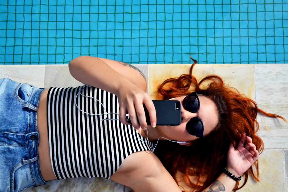 Woman lying next to pool with earphones and phone