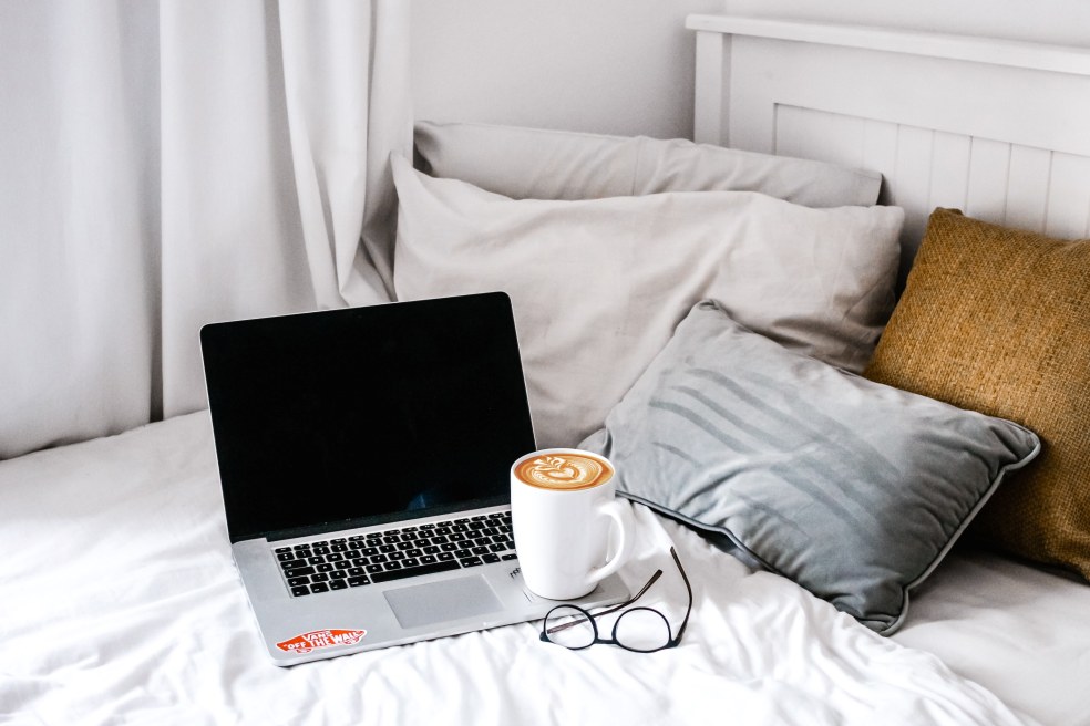Laptop with coffee and glasses on a bed